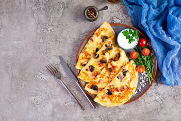 Delicious pancakes with mushrooms, ham and cheese, arugula, tomatoes and sour cream on a wooden background