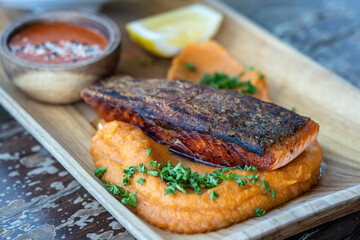 Fried salmon fillets served with vegetable garnish on wooden plate and sauce. Roasted salmon filet with sweet mashed potatoes.