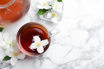 Cup of tea and fresh jasmine flowers on white marble table, flat lay. Space for text