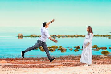 A young man on the seashore runs towards his pregnant wife