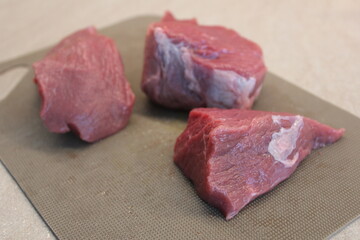 three dark red slices of beef are cut and lie on a light gray background
