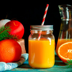 Christmas cocktail. Orange fresh in a glass jar with a tube stands on a wood table next to Christmas toys