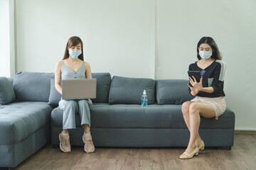 Two young women wearing protective masks using laptops and tablets.