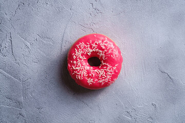 Pink donut with sprinkles, sweet glazed dessert food on concrete textured background, top view