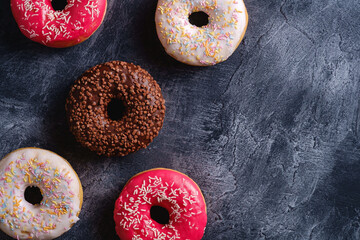 Chocolate, pink and vanilla donuts with sprinkles, sweet glazed dessert food on dark concrete textured background, top view copy space