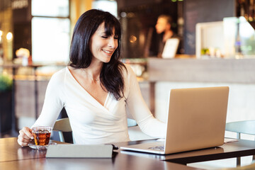 Portrait of a smiling adult woman with laptop in cafe -  smart working concept