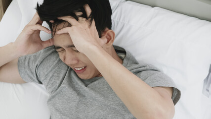 Young man suffering from headache lying on bed at home