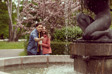 Young, happy, loving couple having date in the park near fountain. Relations, friendship and love.