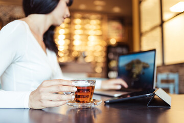 Adult woman sitting in a cafè and using a laptop and a tablet while drinking a cup of tea, smart working concept