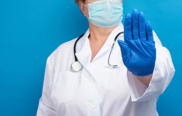 doctor in white medical coat and blue latex gloves shows stop gesture