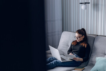 young attractive girl at home working with laptop on the couch. comfort and coziness while at home. home office and work from home. remote online employment.