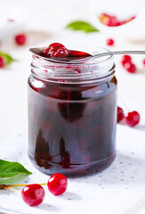 Close-up cherry jam in a glass jar. Homemade sweet cherry jam and fresh cherry on a white table