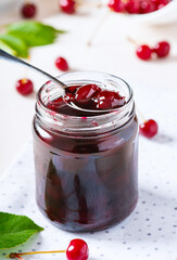 Close-up cherry jam in a glass jar. Homemade sweet cherry jam and fresh cherry on a white table