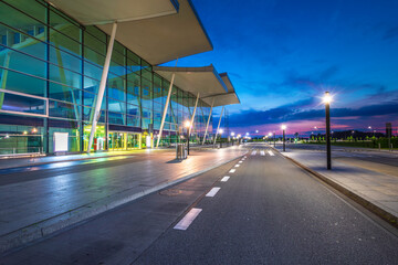 Modern airport terminal at dusk in Wroclaw, Poland. Empty street and no traffic in front of building with sky reflections on glass wall. View on departures and arrivals entrance