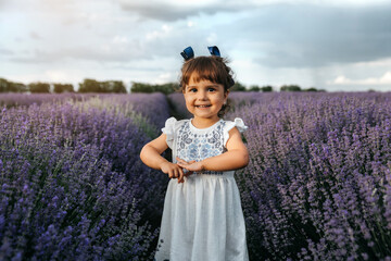 Little happy smiling girl in white dress  is playing in the middle of the lavender field