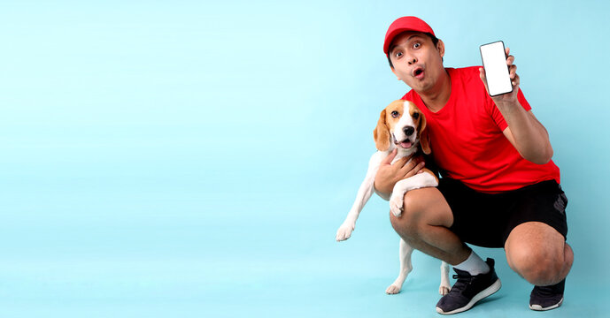 handsome Asian man in red cap and beagle dog,isolated on blue background in studio With copy space. holding mobile phone with blank white empty screen. - Powered by Adobe