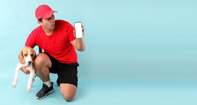 handsome Asian man in red cap and beagle dog,isolated on blue background in studio With copy space. holding mobile phone with blank white empty screen.