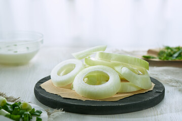 Sliced onion rings on a wooden stand on a white background in blur.
