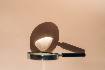 Magnifying glass on a beige background with sun reflection.