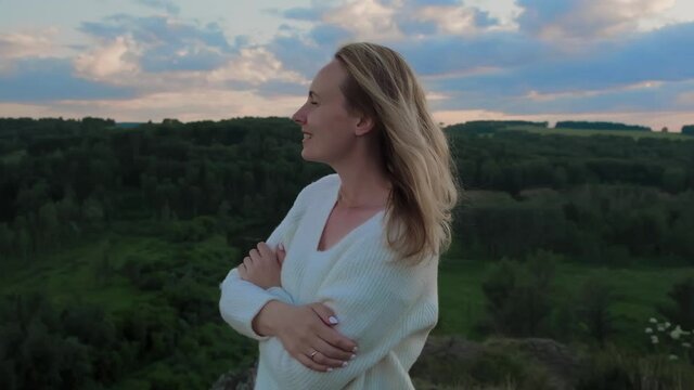 Happy young girl standing on top of a mountain looking at the horizon at sunset. Slow motion.