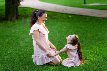 mother and daughter 5-6 years old walking in the Park in the summer, daughter and mother laughing on a bench, the concept of a happy family, the relationship of mother and child, mother's day