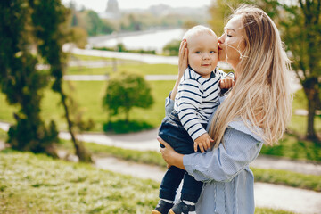 a pretty and a beautiful long-haired mom in a blue dress standing in a solar park and holding on to...