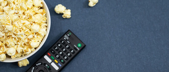 A bowl of popcorn and remote control for TV on a sofa background. concept Leisure and entertainment of watching cinema, top view with space for text. 
