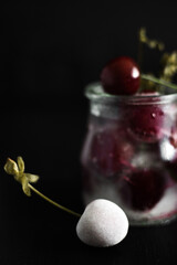 Close-up Front view of frozen sweet cherry and a glass jar full of frozen fruits nearby on a black background, still life vertical picture