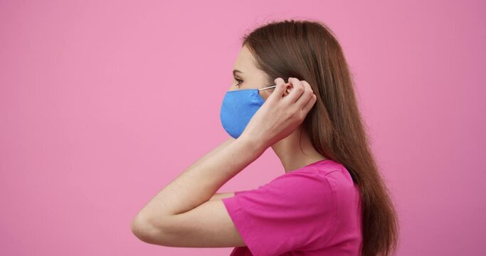Side view of cute young girl with dark hair wearing blue medical mask to protect herself from coronavirus. Isolated over pink studio background. Concept of prevention and health care.