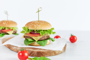 Beef burger with fresh salad, cheese and tomatoes on white table.