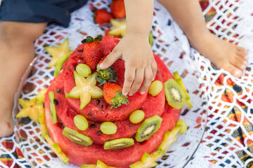 Close em mão de criança que está brincando com frutas em formato de bolo de aniversário.