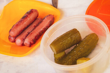 Grilled sausages and pickles in plastic dishes. Disposable tableware
