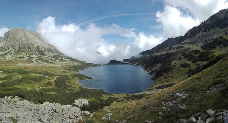 Mountains glen filled with silent crystal clear lake and opening on blue sky and calm clouds