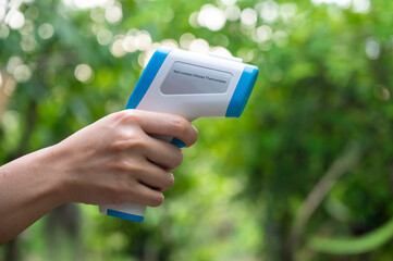 Hand holding a non contact infrared thermometer on blurred park background 