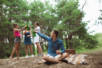Naklejka na ściany i meble Togetherness. Group of friends clinking beer bottles during picnic in summer forest. Lifestyle, friendship, having fun, weekend and resting concept. Looks cheerful, happy, celebrating, festive.
