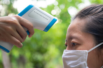Close up of Asian woman wearing white face mask being measured body temperature by using non...