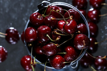 Flat lay view of a red sweet cherries in a metal bucket on grey background. Summer taste. Fresh berries under the water drops