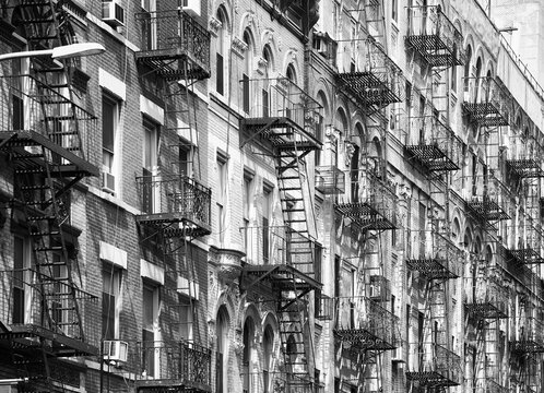 Black and white picture of Manhattan old residential buildings with fire escapes, New York City, USA.