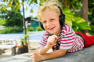 Young positive child in headphones listening music with fun at tropical beach party. Travel family lifestyle, recreational activities at summer cruise vacations.
