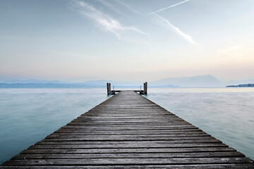An old wooden pier extends into the clear blue waters of the lake. A solitary path towards the calm...