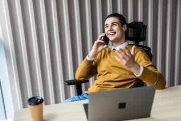 Young businessman working at the computer talking on the phone and smiling