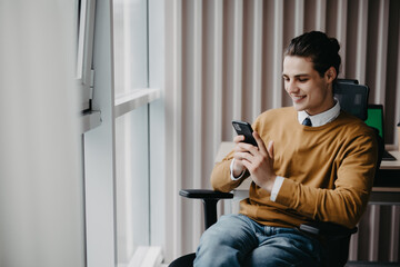 Young man workingtaking smartphone in hand, smiling in office