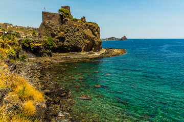 Fototapeta na wymiar A view along the seafront in Acicastello, Sicily showing the Norman castle and the islets of Acitrezza in summer