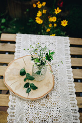 Blumen in einer Vase auf einem Holzbrett auf einer Häkeldecke. 