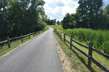 Fototapeta na wymiar Scenic footpath and bicycle trail at Thompson Park in Holmde, New Jersey, USA, on a mostly sunny day with puffy cumulus clouds