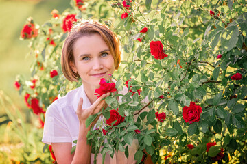 portrait of a young woman among red roses in the back sunlight