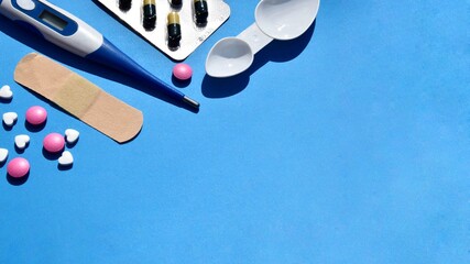 Electronic thermometer, pills or vitamins on a blue background. Top view on a dark blue background. Protection against viruses, coronaviruses, flu, colds, diseases. Health concept.