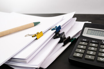 A pile of unfinished documents, a calculator and a pen on an office desk, a desk made of business paper. Close-up.