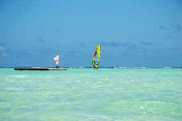 Picture of a deck in the turquoise water and a person windsurfing with a yellow sail on the Caribbean Ocean in Bonaire