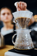 Professional barista girl brewing coffee in a drip way through a paper filter in a purover dripper